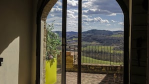 Vista a través de un arco con portón metálico, que da a un balcón con vistas a un paisaje rural con colinas ondulantes y cielo parcialmente nublado.