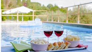 Escena junto a la piscina con dos copas de vino tinto, un bol de palomitas y un plato de panecillos.