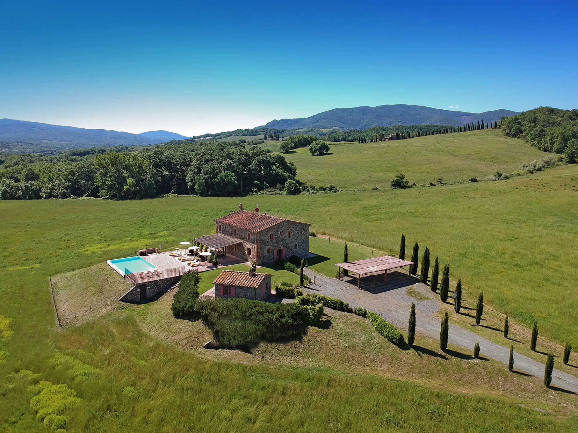 A stone villa with a swimming pool, surrounded by a well-maintained lawn and cypress trees.