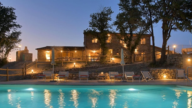 Ein Gebäude aus Stein mit Pool, Liegestühlen und Beleuchtung im Freien.