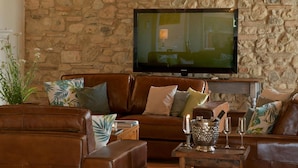 Ein Wohnzimmer mit Steinwand, Ledersofas, einem Flachbildfernseher und einem kleinen Holztisch mit Kerze und Gläsern.
