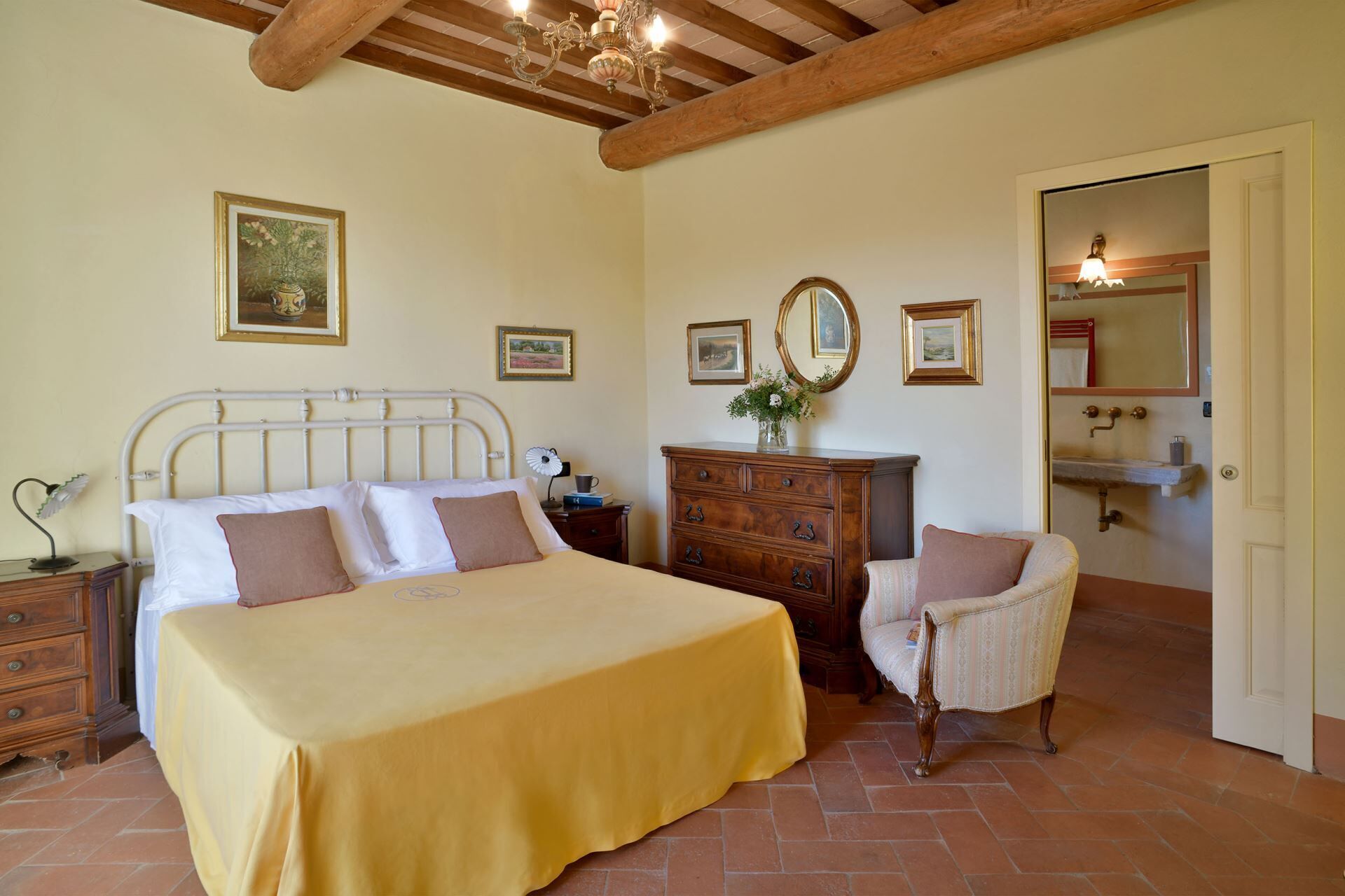 Ein Schlafzimmer mit Bett, Schminktisch, Stuhl und einem durch eine offene Tür einsehbaren Badezimmer.