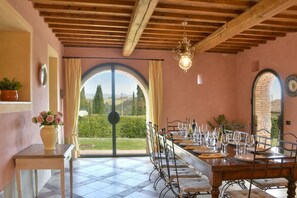 A dining area with a long table set for six, a chandelier, and a view of the countryside through an arched window. - Magnificent stone house 10 km from the sea with solarium and heated pool. (Guardistallo)