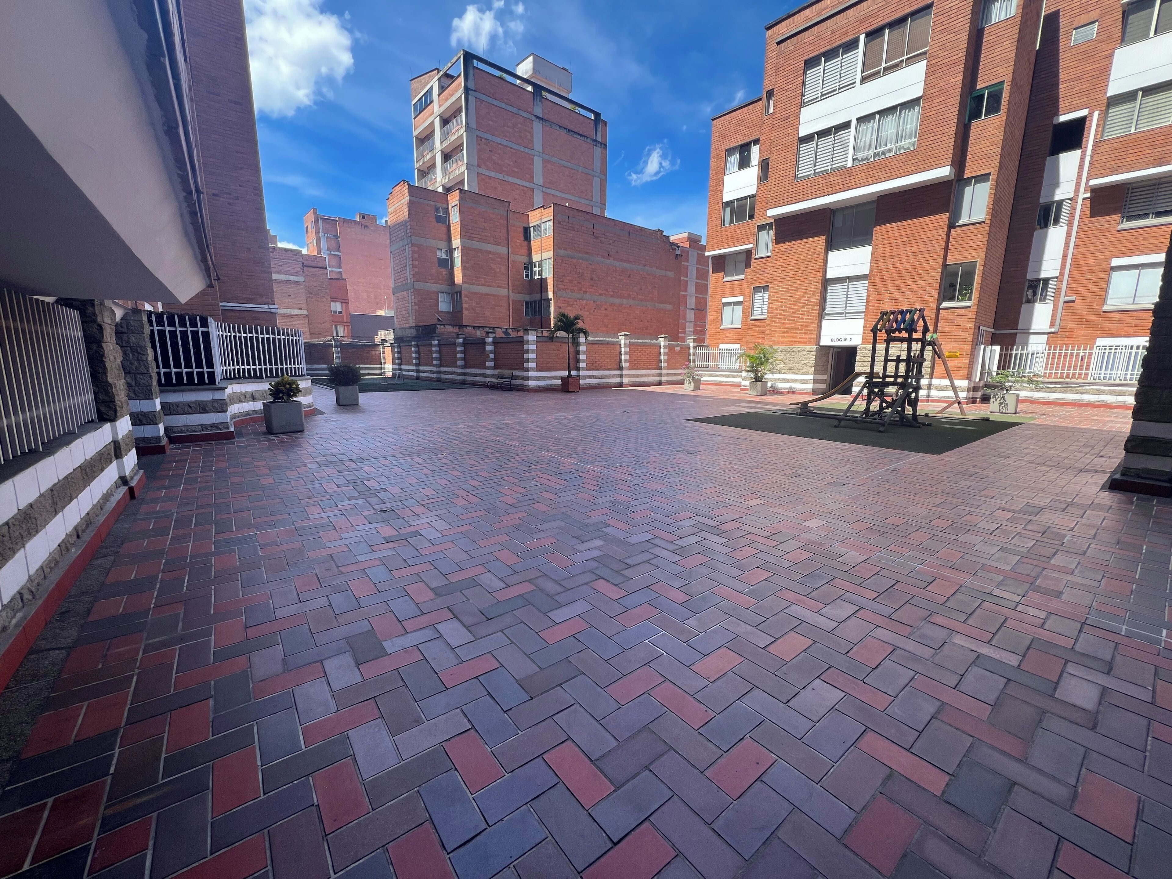Un patio con suelo de ladrillo, rodeado de edificios de varios pisos con balcones y ventanas.