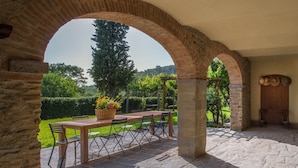 An outdoor patio with a stone table and chairs, surrounded by stone arches, and a view of a lush garden. - Podere della Rosa: elegance and comfort in the Tuscan hills (Arezzo)