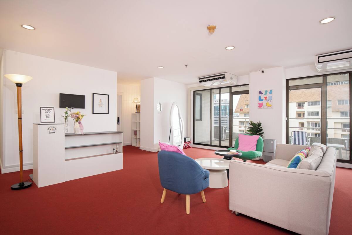 A modern living room with a red carpet, a blue chair, a white sofa, and a large window with a city view.