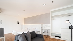 A modern living room with a grey sofa, a white bed, and a white wardrobe. - Bed to Bliss (Bangkok)
