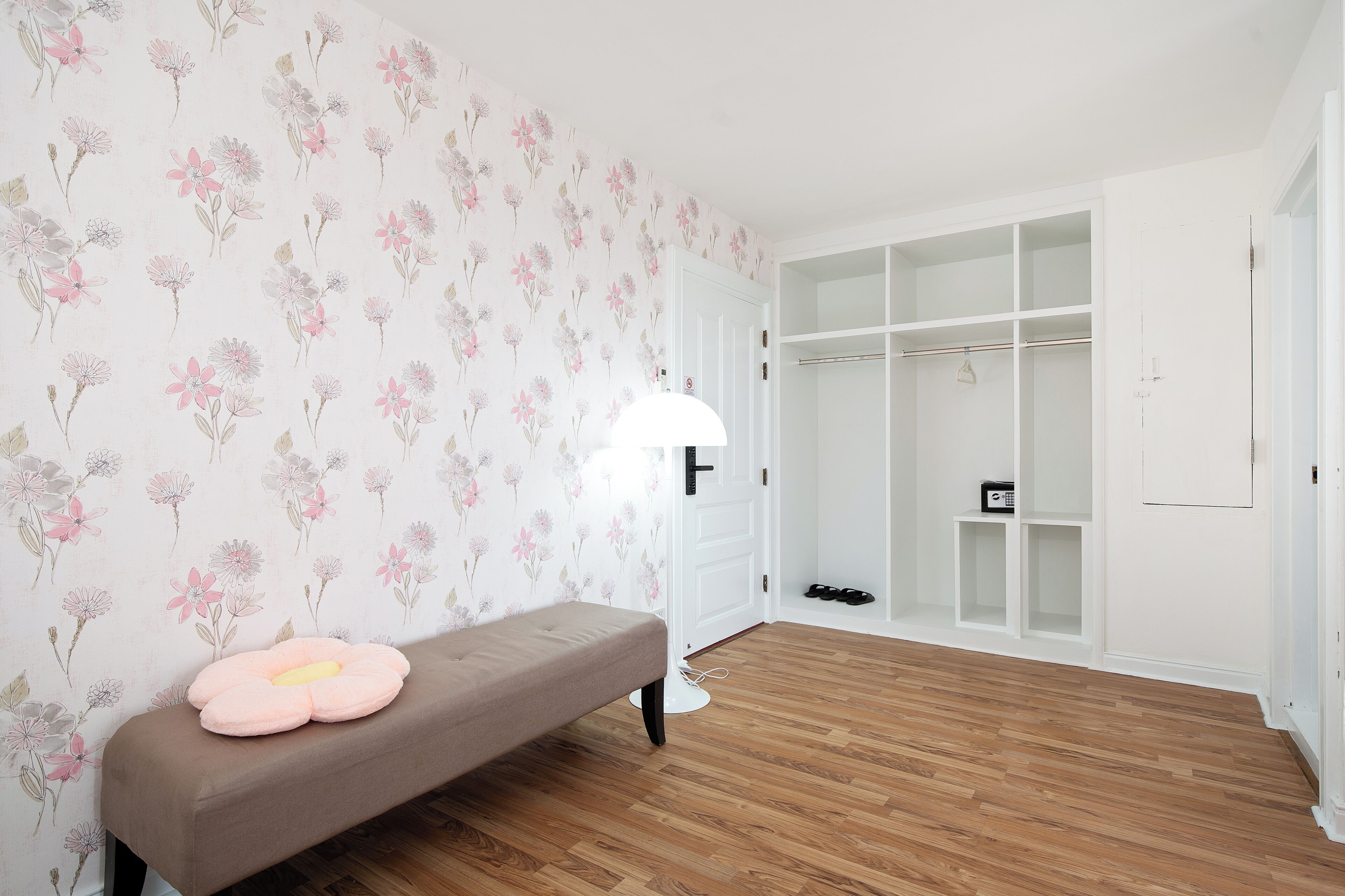 A room with a wooden floor, a bench with a pink cushion, a white door, and a closet with shelves.