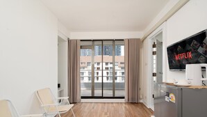 A modern hotel room with a large sliding glass door leading to a balcony, a flat-screen TV, a refrigerator, and a seating area with chairs. - Bed to Bliss (Bangkok)