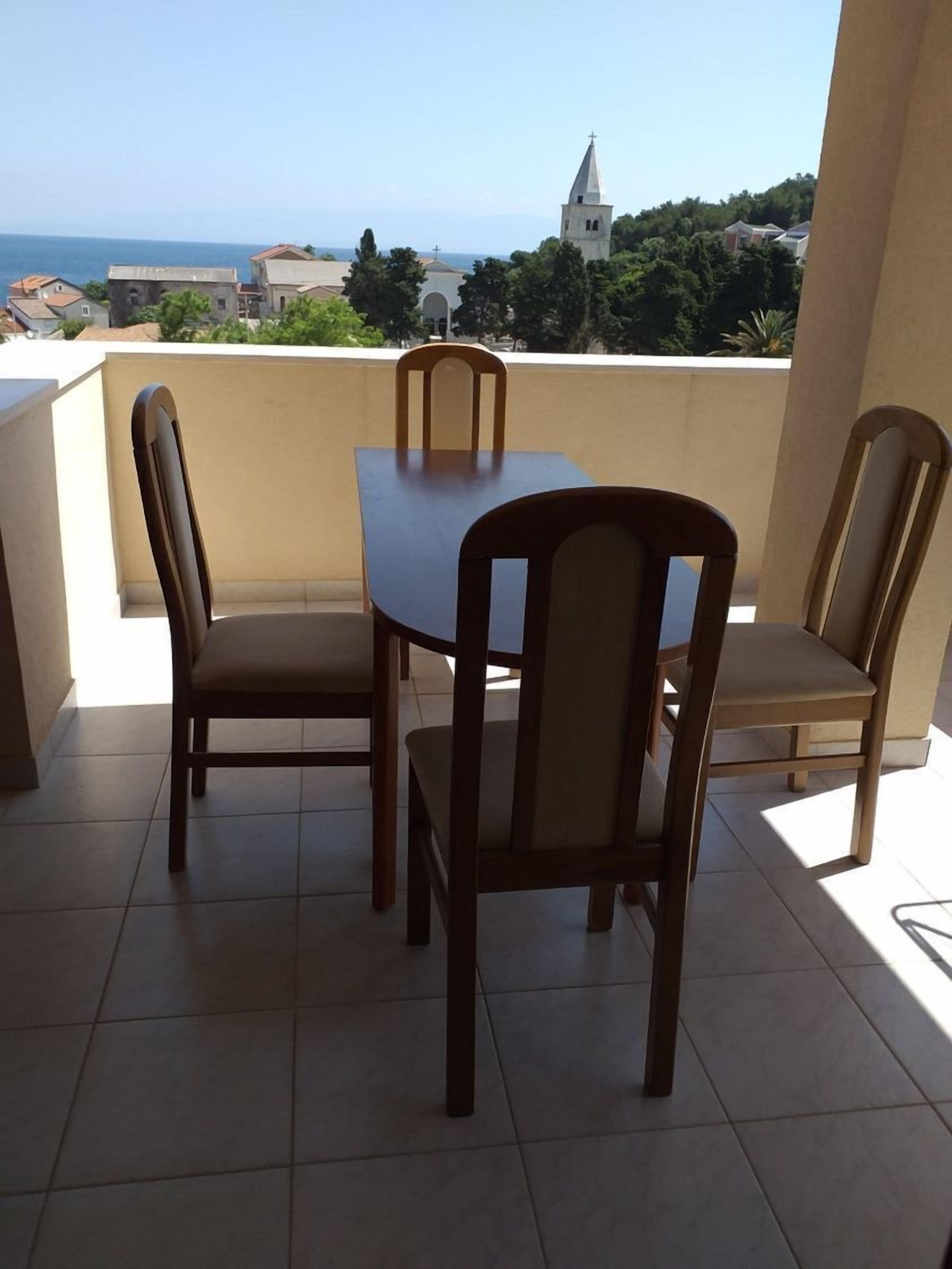 A balcony with a table and chairs, a view of the sea, and a church in the background.