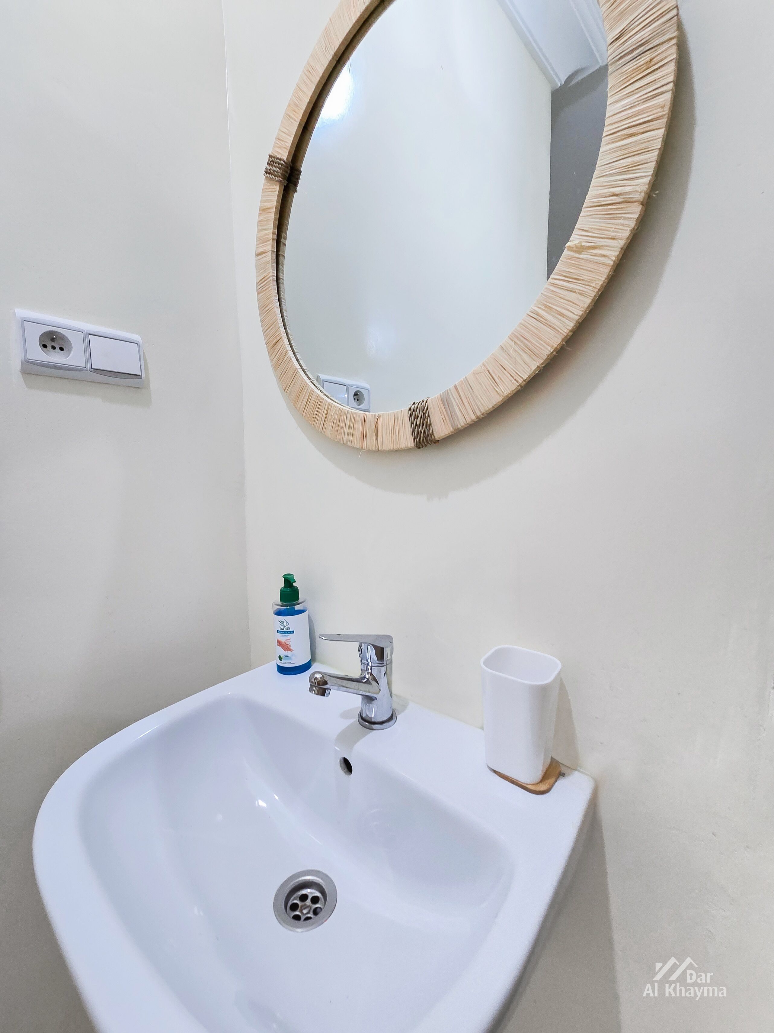 A bathroom with a white sink, a mirror with a wooden frame, a faucet, a soap dispenser, and a cup.