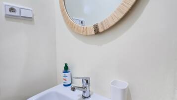 A bathroom with a white sink, a mirror with a wooden frame, a faucet, a soap dispenser, and a cup.
