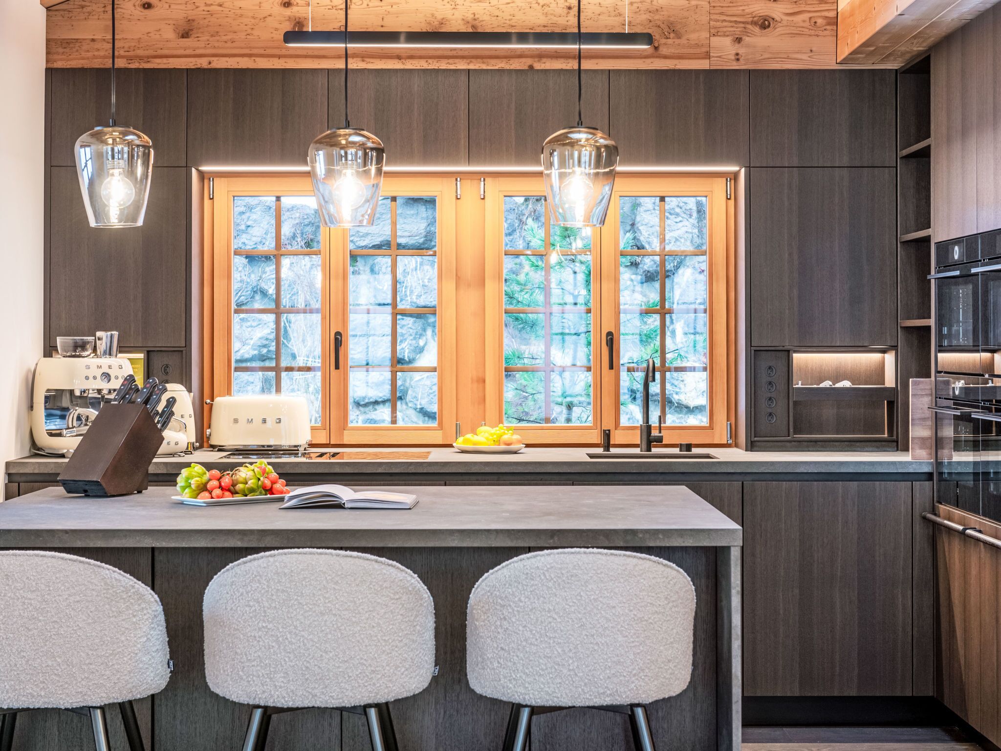 Une cuisine moderne avec des meubles en bois, une grande fenêtre à vitrage dépoli et un îlot central doté de tabourets de bar.