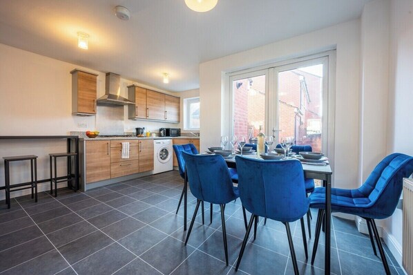 A modern kitchen with a dining area, featuring a large window, dark tiled flooring, and blue chairs.