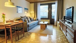 En hyggelig stue med en sofa, spisebord, fjernsyn og et vindue med udsigt til bygninger.