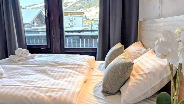 Et hotelværelse med to senge, udsigt til et bjerrelandskab og en balkon med gelænder.