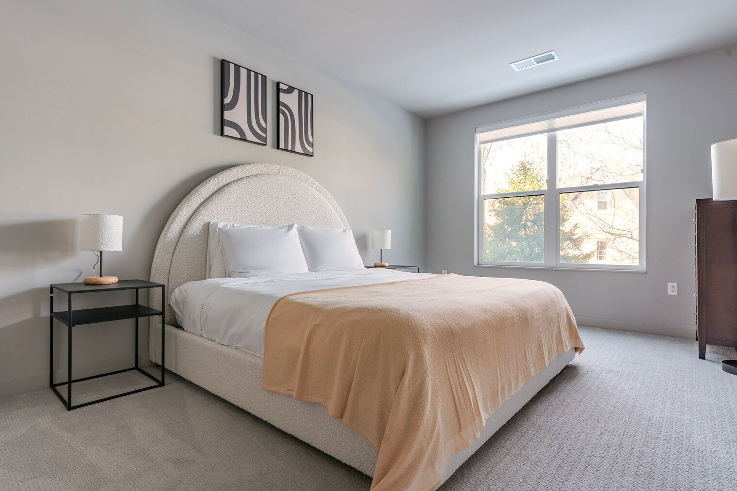 A bedroom with a bed, two bedside tables, a window, and artwork on the wall.