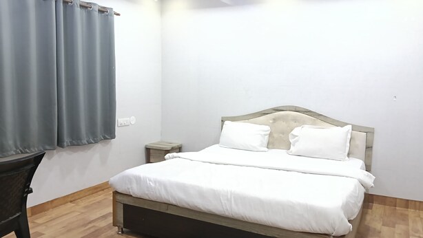 A single bed with a wooden headboard, white bedding, a small bedside table, and a grey curtain. - Aryan (Bhubaneshwar)