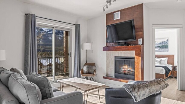 Una sala de estar moderna con chimenea, televisor y balcón con vistas panorámicas a la montaña.