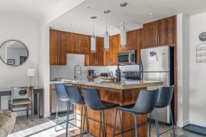 A modern kitchen with wooden cabinets, stainless steel appliances, and bar stools. - Serene 2BR Hideaway Hot Tub + Breathtaking Views (Canmore)