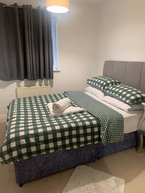 A neatly made bed with checkered bedding, a rolled towel, and a bedside table with a lamp. - Aberdeen City Escape Apartment (Aberdeen)