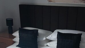 A neatly made bed with white linens and two dark pillows, a wooden headboard, and a nightstand with a lamp. - Aberdeen City Escape Apartment (Aberdeen)