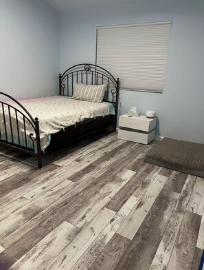 A bedroom with a metal bed frame, a wooden floor, a bedside table with a lamp, and a window with blinds. - Townhouse just outside of Denver (Littleton)