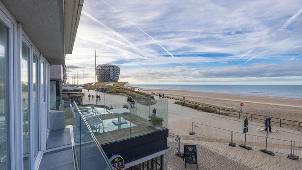Vista desde un balcón con vista a una playa y un edificio esférico distintivo al fondo.