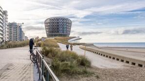 Un paseo marítimo con una estructura arquitectónica moderna, una playa y una bicicleta.