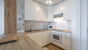 Una cocina moderna con armarios blancos, encimera de madera, microondas integrado y pileta de acero inoxidable.