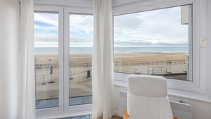 Una habitación con un ventanal grande que da a una playa, una silla blanca y vistas a la playa y al mar.