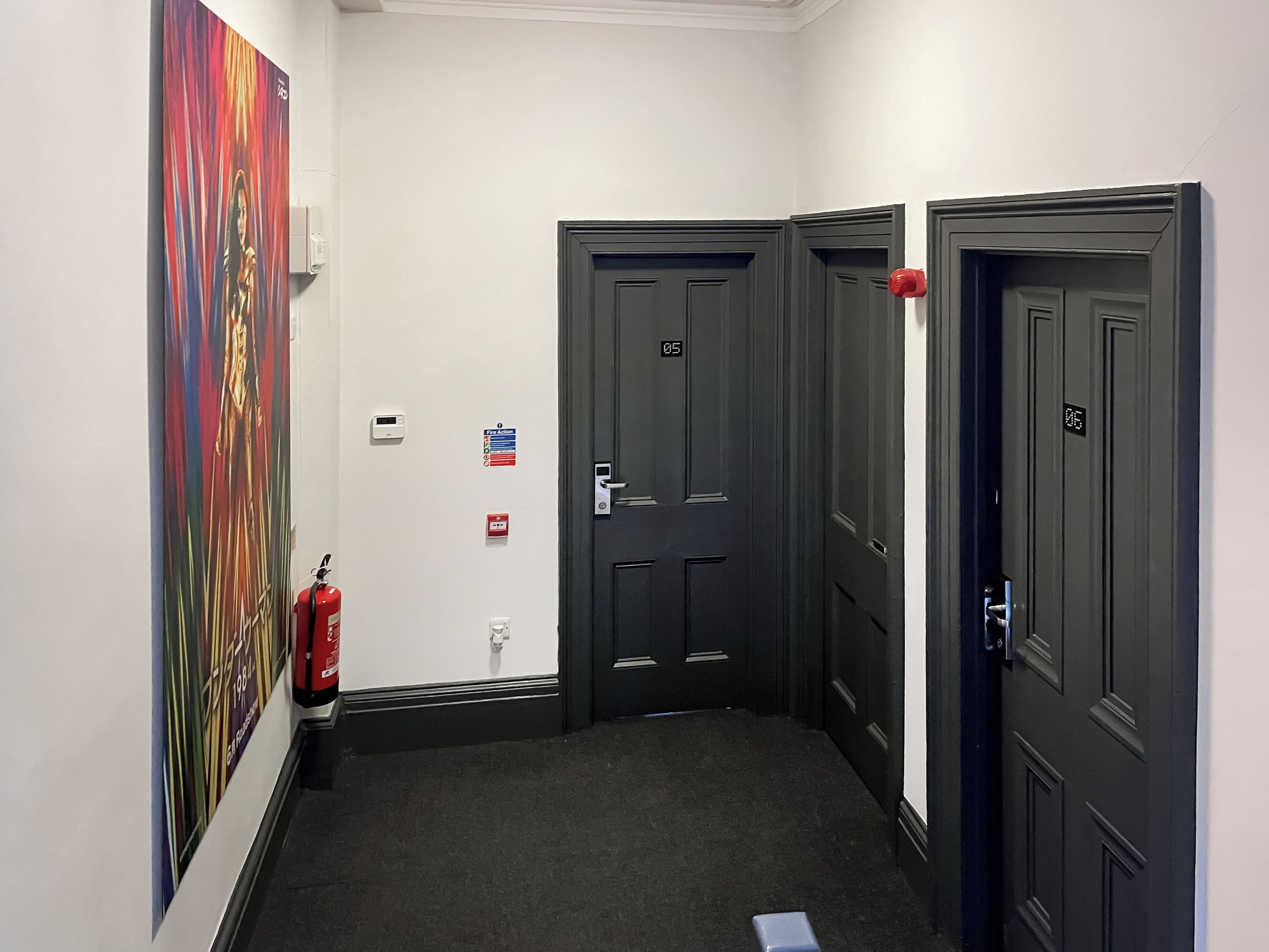 A hallway with three doors, a fire extinguisher, and a fire action sign.