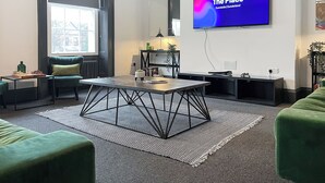 A modern living room with a large flat-screen TV, a chessboard, a sofa, a coffee table, and a patterned rug.