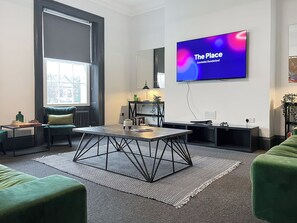 A modern living room with a large flat-screen TV, a chessboard, a sofa, a coffee table, and a patterned rug.