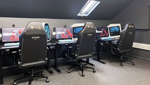 A gaming setup with multiple monitors, chairs labeled 'TITAN,' and a ceiling light.