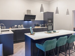 A modern kitchen with dark cabinetry, a central island with bar stools, pendant lighting, and a built-in oven.