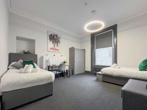 A modern hotel room with two beds, a desk, a chair, a radiator, and a poster on the wall.