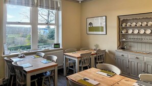 A dining area with a wooden table and chairs, a radiator, a window with curtains, a wall-mounted shelf with plates, and a framed picture. - 5 bedroom accommodation in Baildon (Baildon)