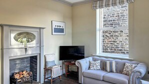 A living room with a fireplace, a television, a sofa, and a window with a stone wall. - 5 bedroom accommodation in Baildon (Baildon)