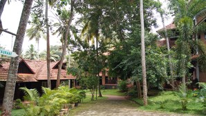 A courtyard with a cobblestone path, surrounded by lush greenery and palm trees.