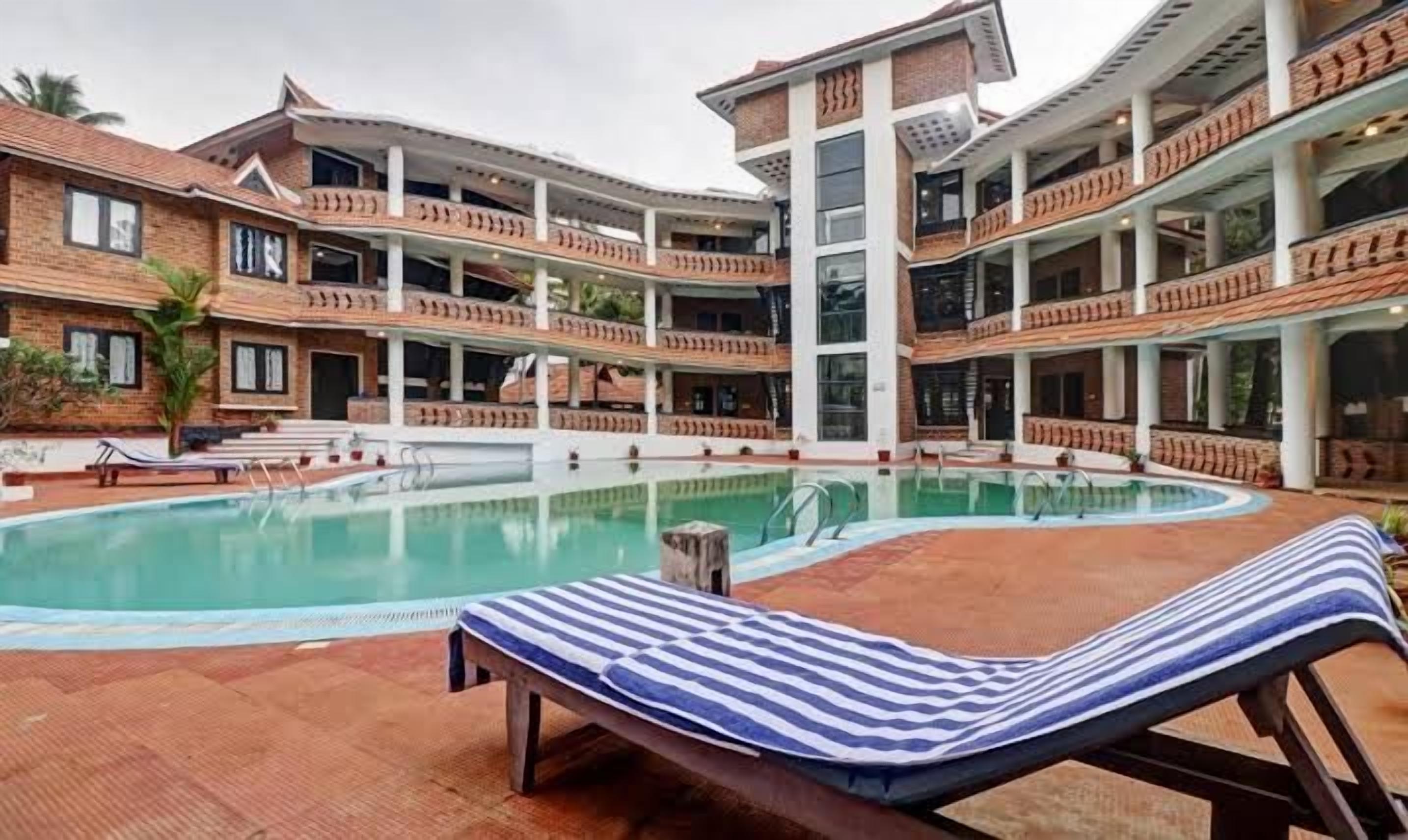A pool area with lounge chairs and a multi-story building with balconies.