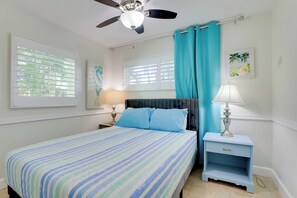 Ein Schlafzimmer mit Bett, Nachttisch, Deckenventilator und einem Fenster mit Jalousien.