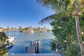 A marina with boats docked, a wooden pier, and a backdrop of houses and palm trees. - 1 Block to Beach! Boutique Condo at John’s Pass (Madeira Beach)
