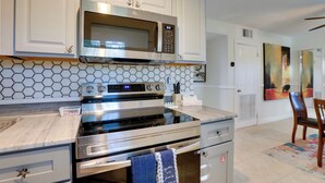 Una cocina moderna con armarios blancos, un microondas de acero inoxidable, un horno doble y una encimera de mármol.
