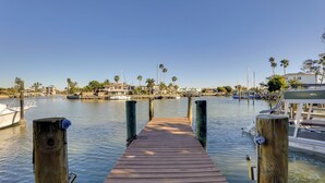 Un muelle de madera que conduce a un puerto deportivo con barcos y casas al fondo.