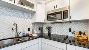 A kitchen with white cabinets, a stainless steel sink, a microwave, and a woven basket with utensils.