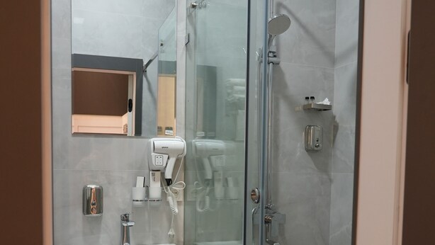 Un baño moderno con ducha de vidrio, lavamanos pedestal y espejo sobre el lavamanos.