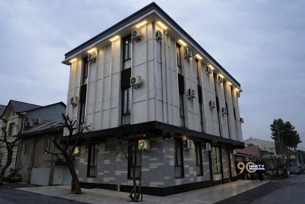 Un edificio moderno con fachada de azulejos, varias unidades de aire acondicionado y un cartel que indica que es el Ninety Boutique Hotel.