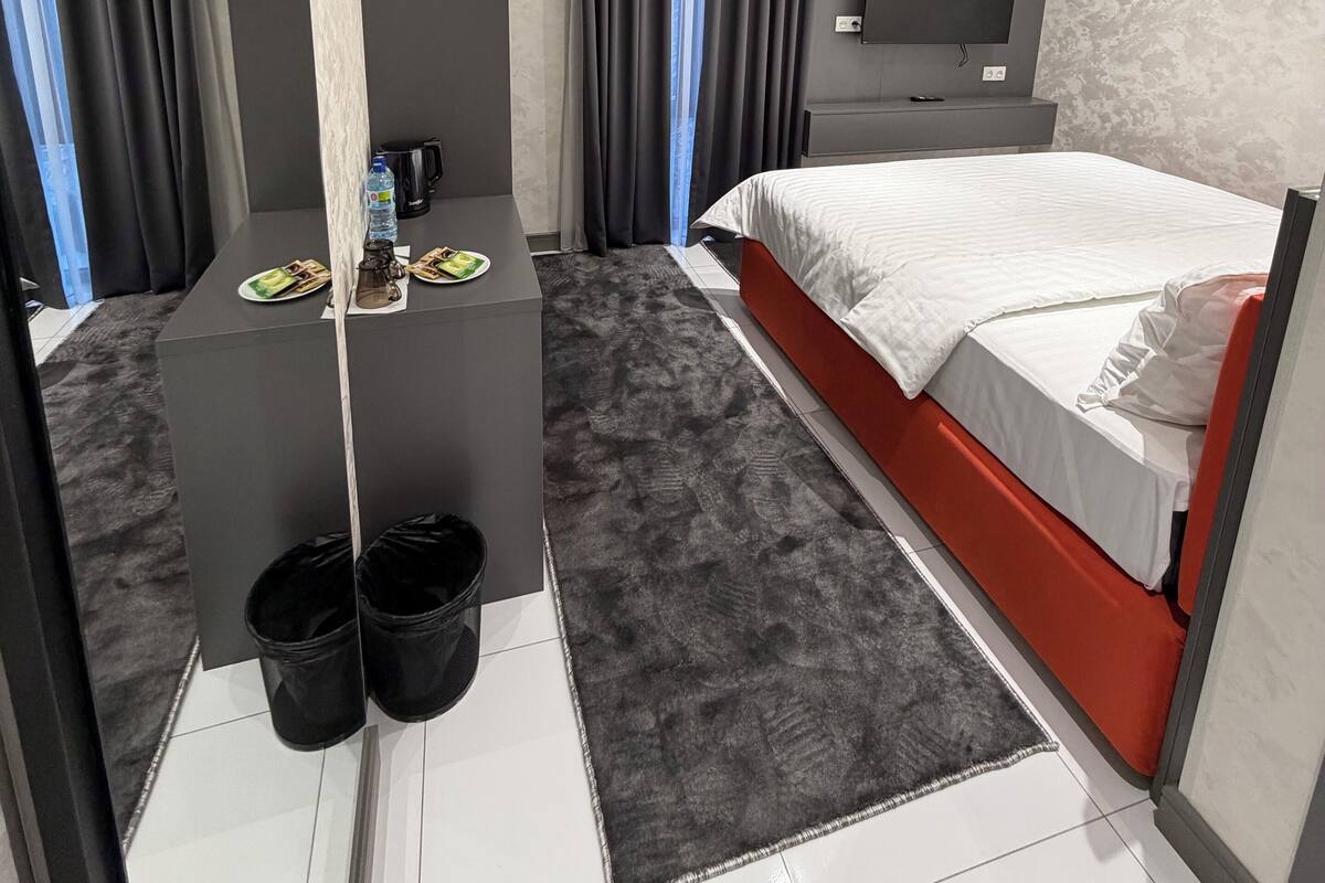 Ein modernes Hotelzimmer mit einem Bett, einem kleinen Schreibtisch, einem Fernseher und einem Fenster mit Vorhängen.
