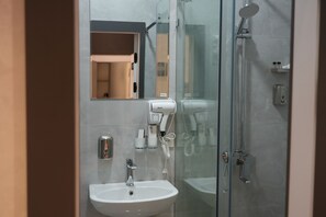Un baño moderno con cabina de ducha de vidrio, lavamanos blanco y secador de pelo de mano fijado a la pared.